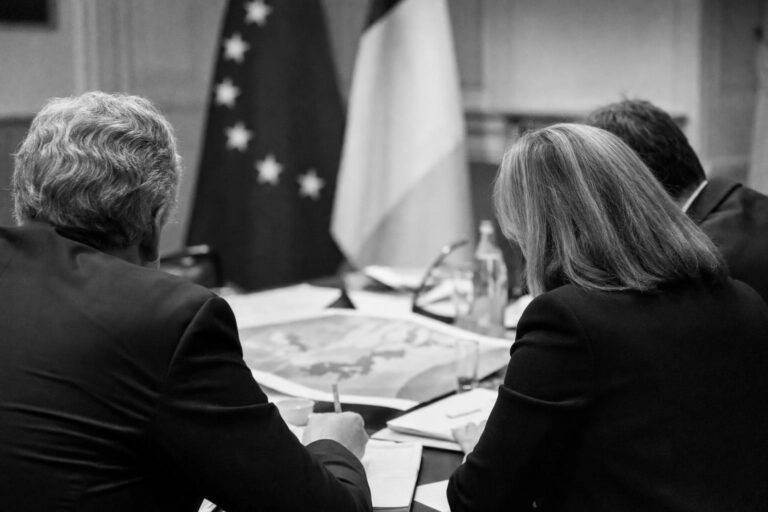 Réunion de travail vue de dos, drapeaux européen et français en arrière-plan